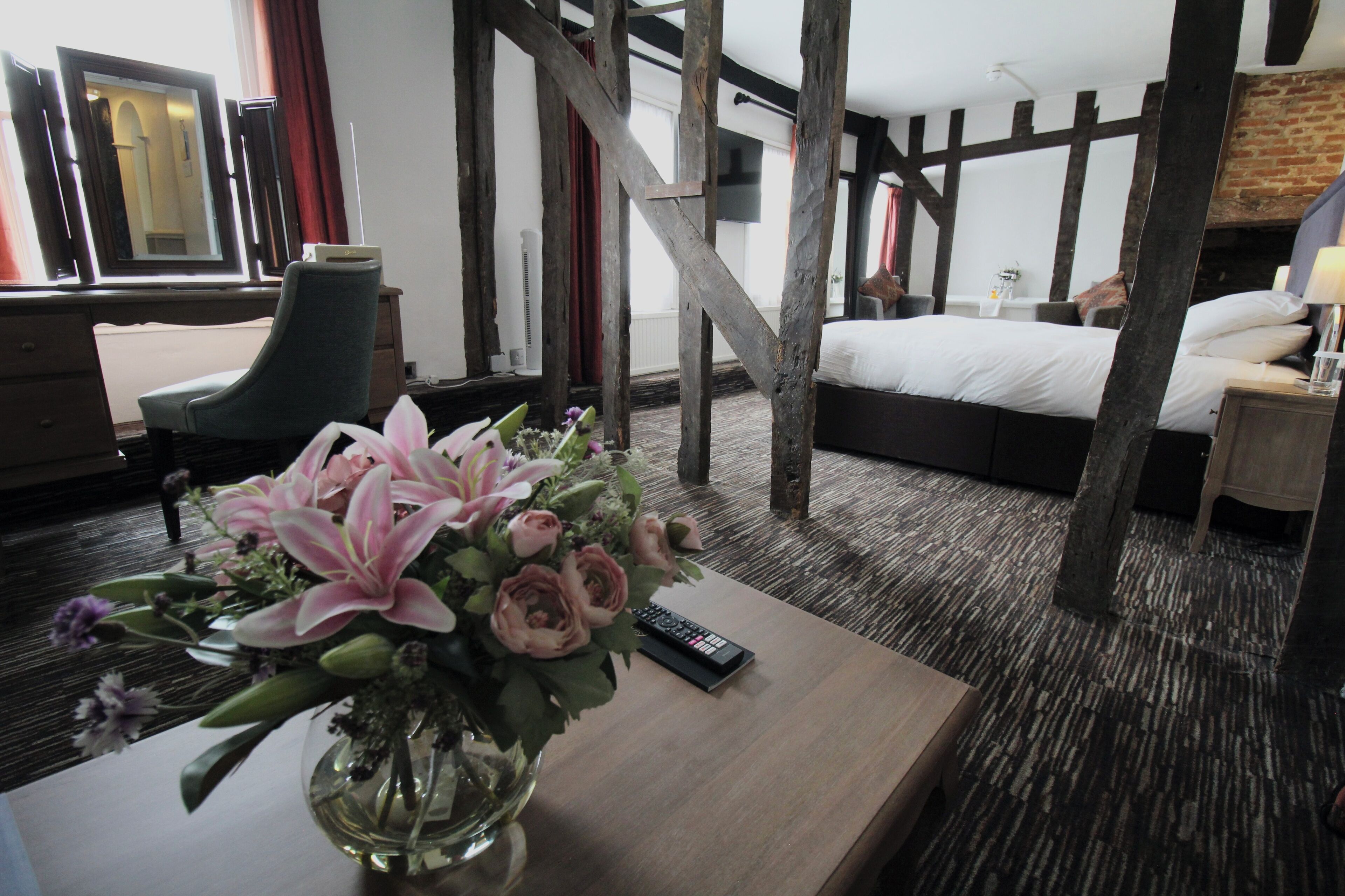 Une chambre d’hôtel avec un plafond en bois, un lit, un bureau agrémenté d’un vase de fleurs et une chaise.