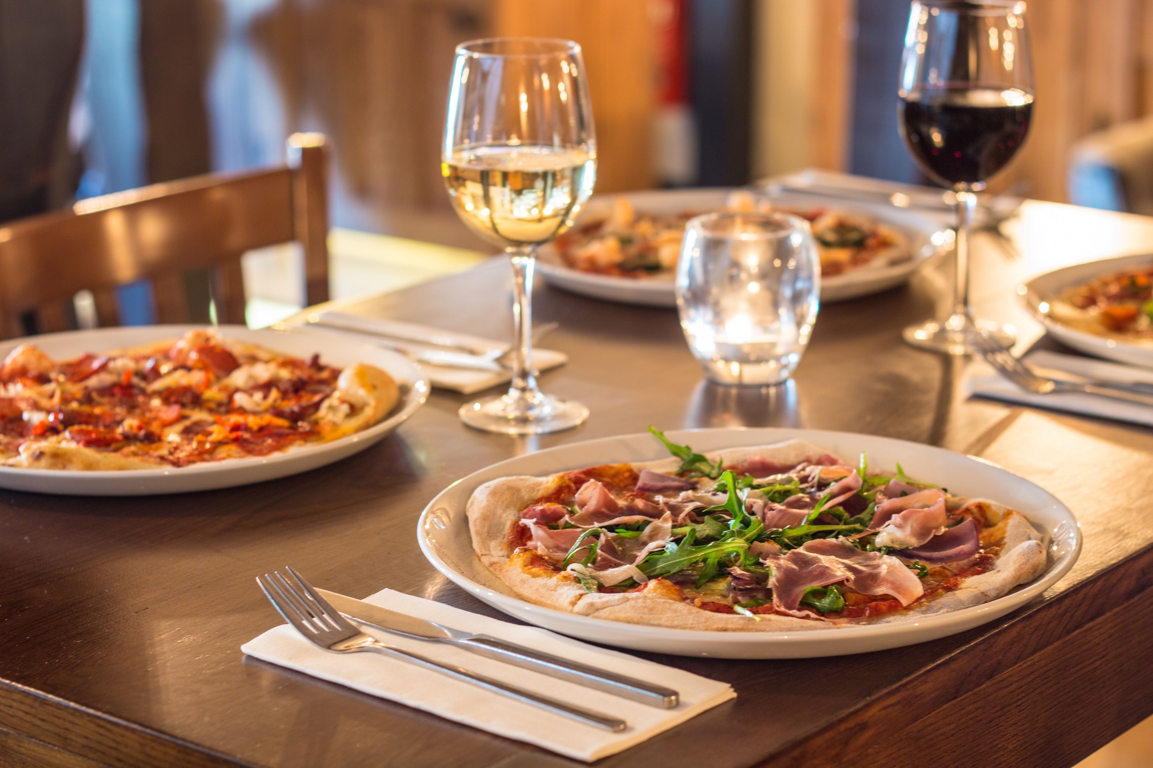 Une table à manger avec des assiettes de pizza, des verres d’eau et de vin, et des couverts.