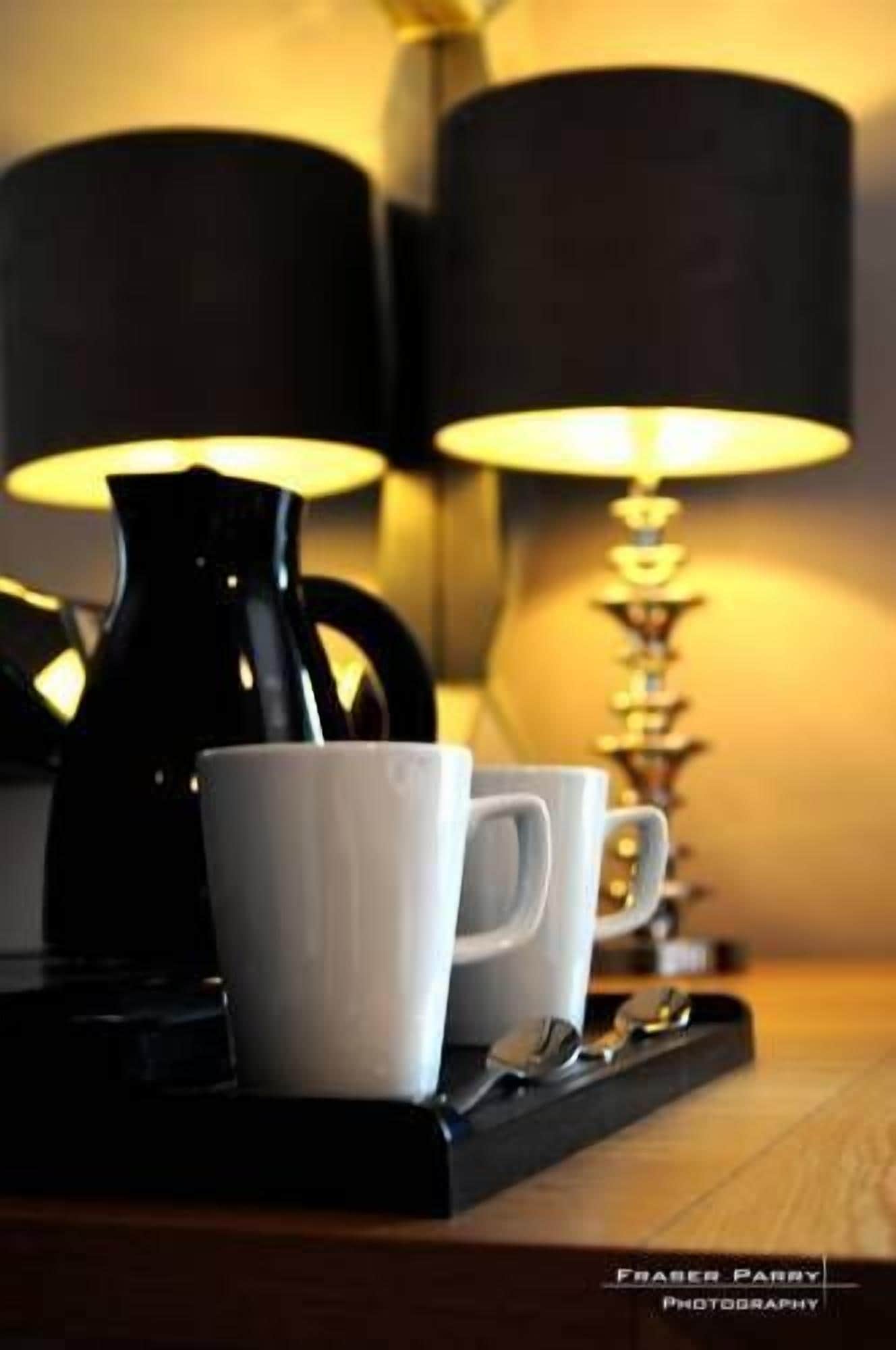A tray with two white mugs, a black coffee pot, and a spoon on a wooden surface.