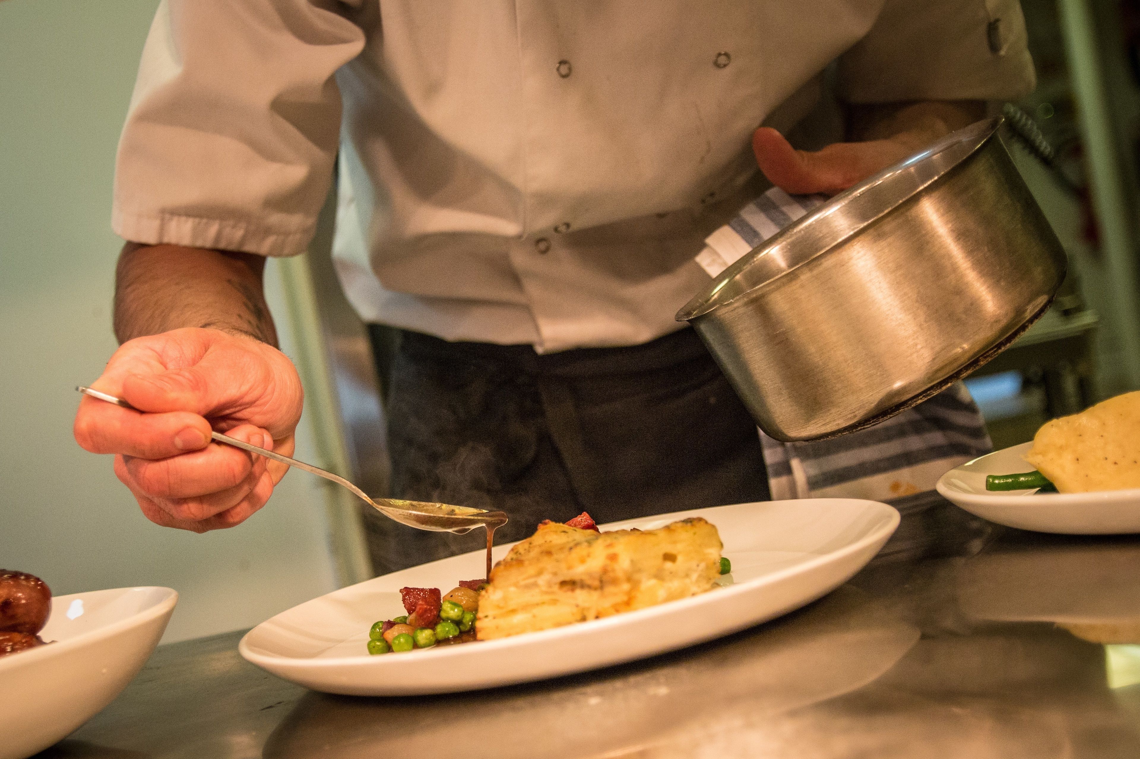 Un chef verse une sauce sur un plat contenant des petits pois et de la viande.
