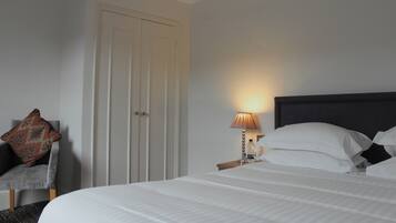 A neatly made bed with white linens, a bedside lamp, and a chair with a patterned cushion.