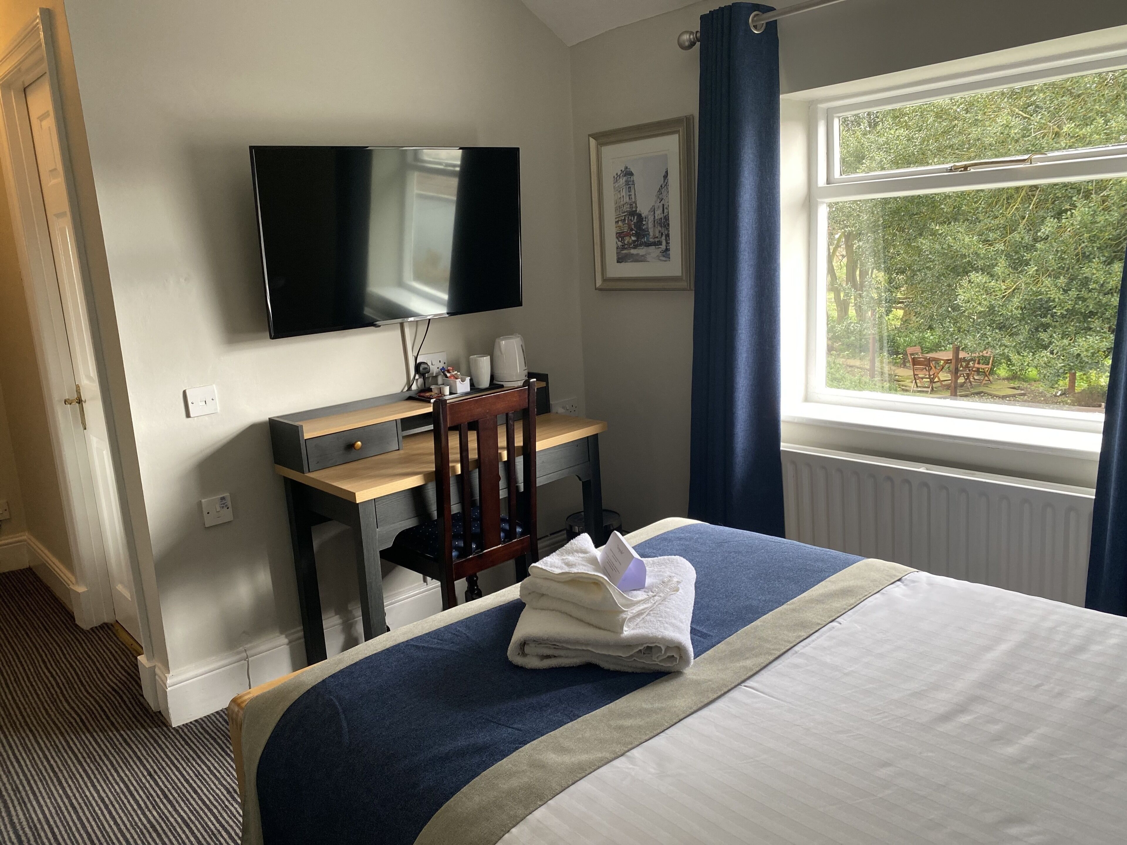 Quarto de hotel com cama, escrivaninha, televisão e janela com vista para áreas verdes.