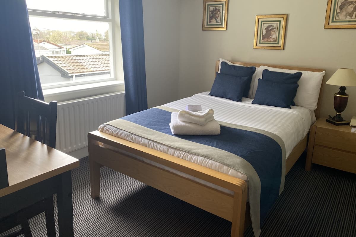 Quarto de hotel com cama, escrivaninha e janela.