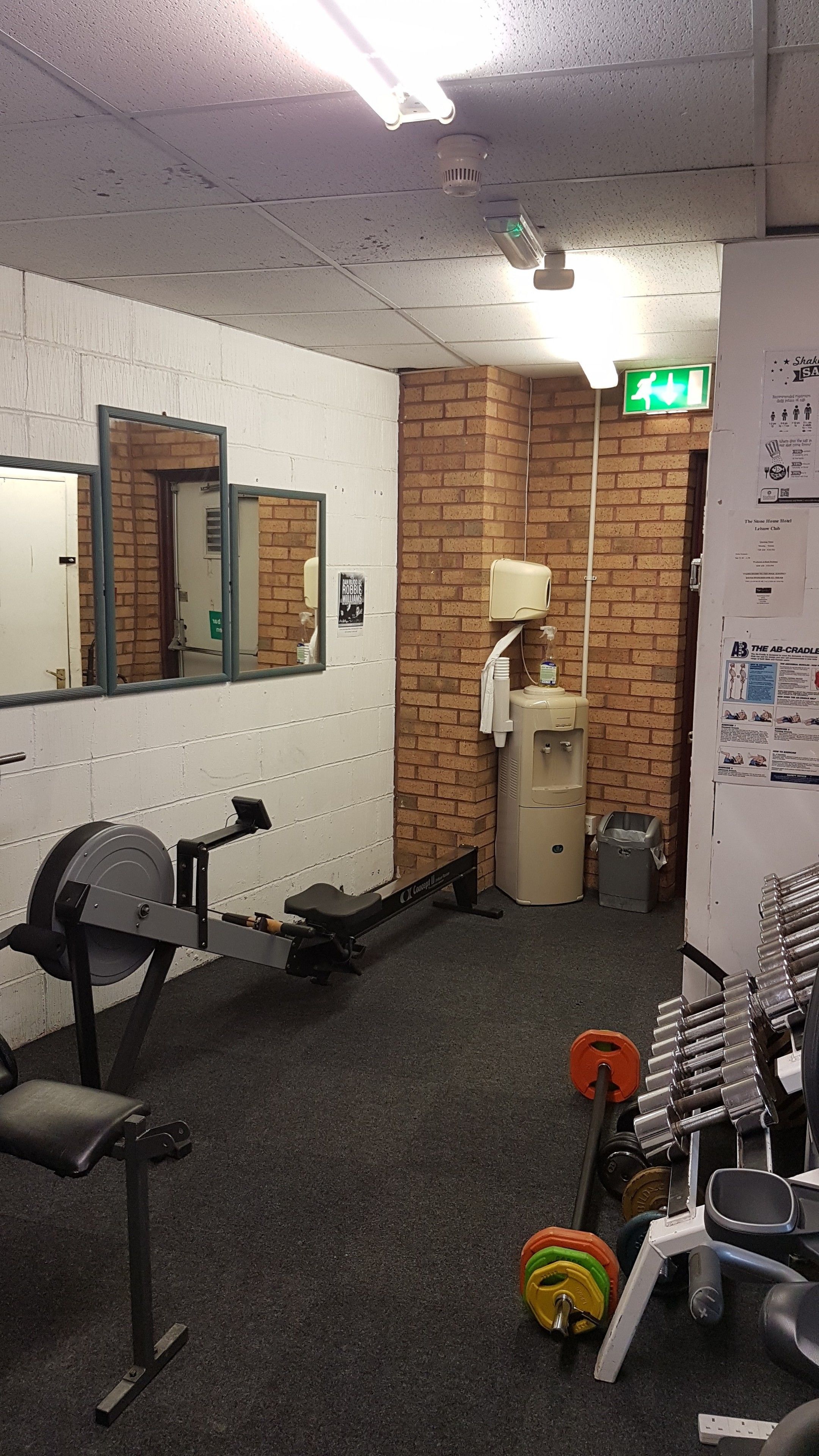 A gym with exercise equipment, a mirror, a water dispenser, and a brick wall.