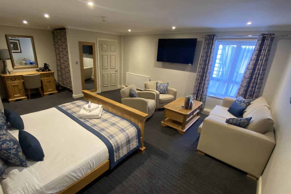 Quarto de hotel com uma cama, um sofá, uma escrivaninha e uma televisão.