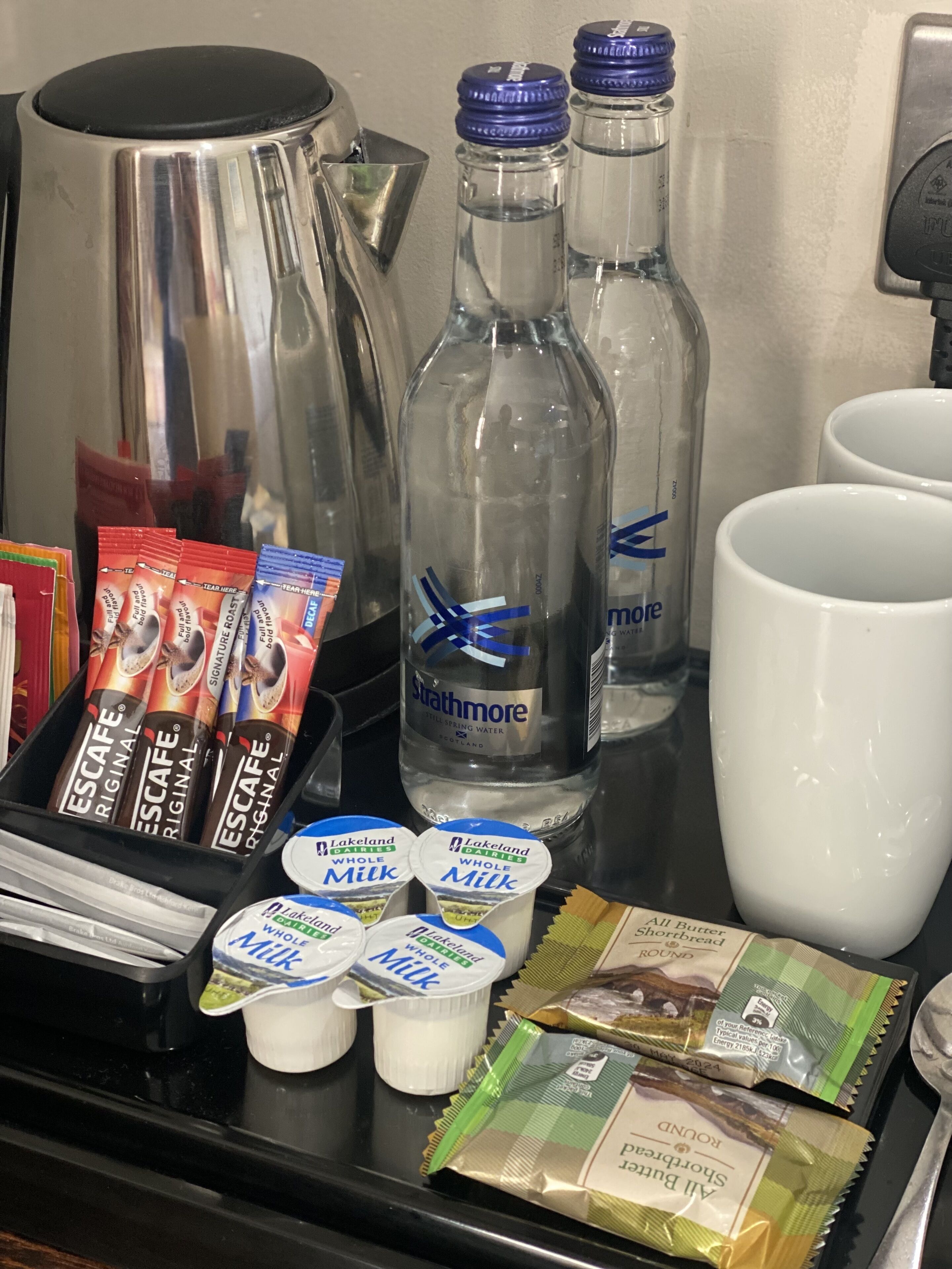 Bandeja de desayuno con café, agua embotellada, leche y pasteles.