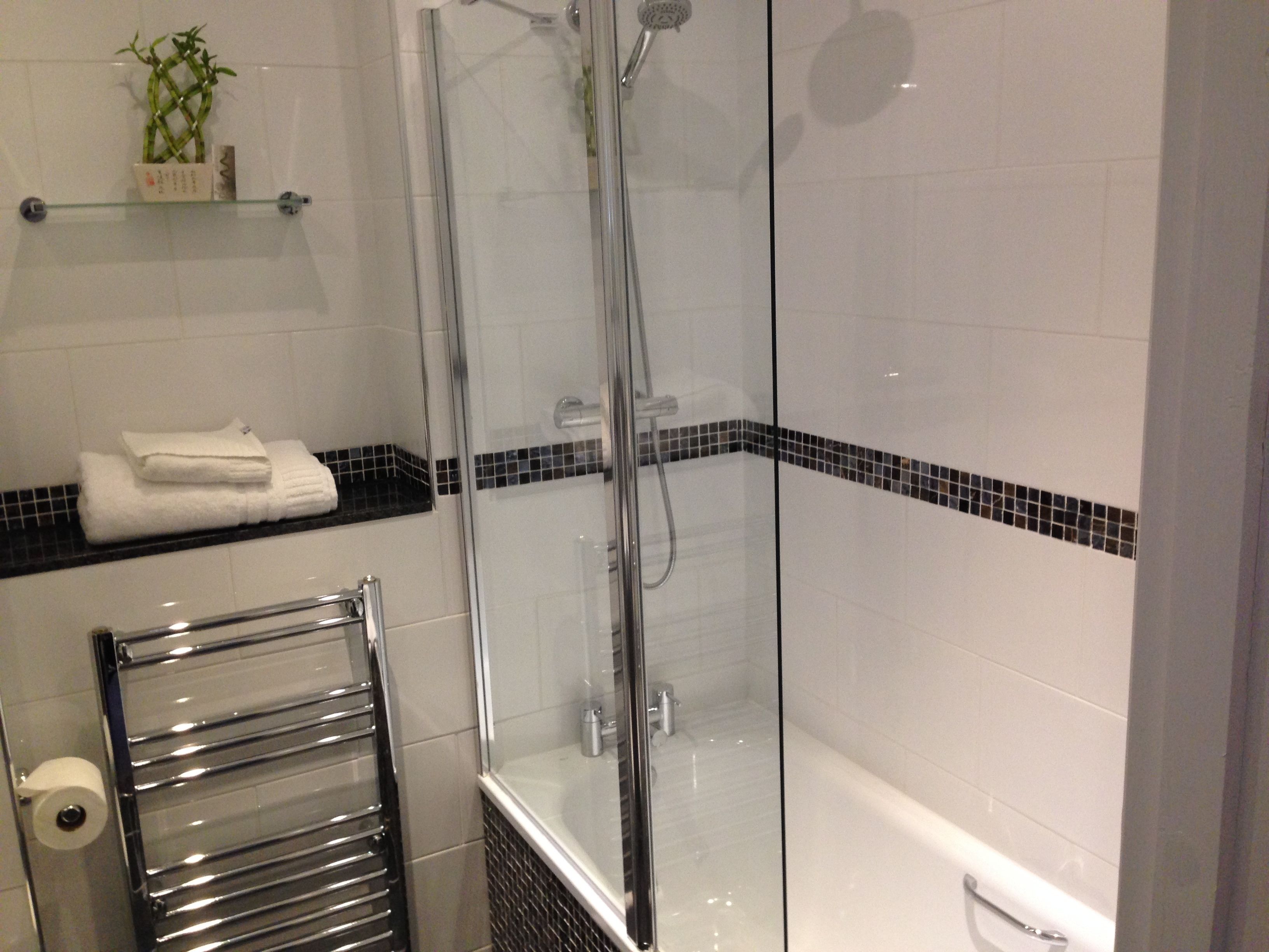 Un baño moderno con ducha de mampara de vidrio, una bañera blanca y un perchero para toallas.