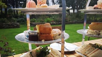 Una bandeja de tres niveles al aire libre con sándwiches, scones y un postre sobre una mesa de madera en un jardín.