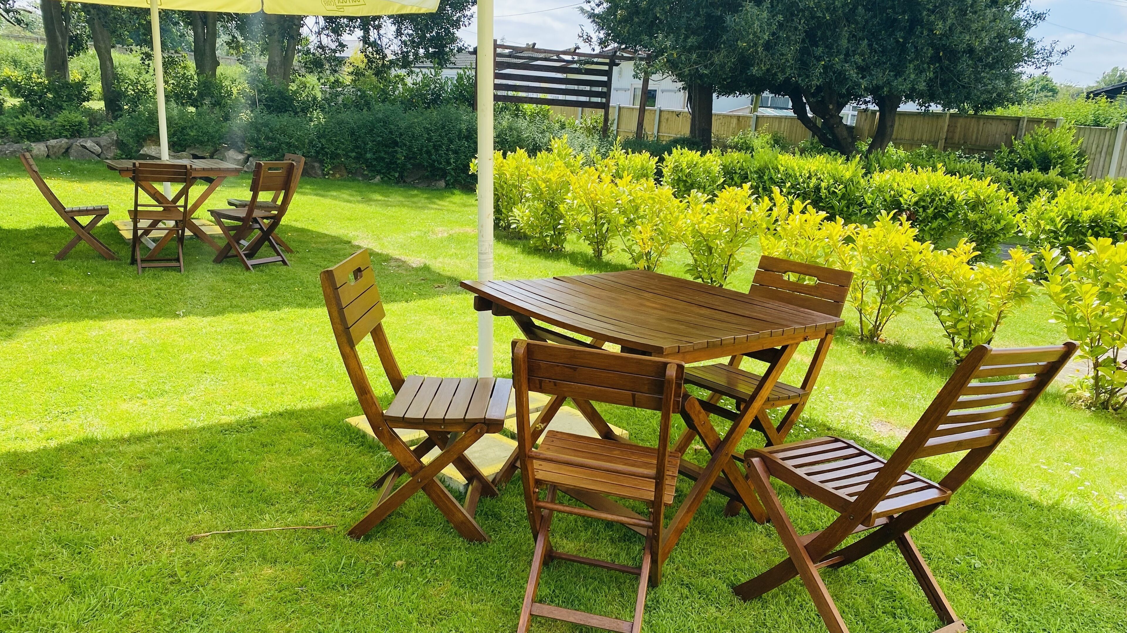 A wooden outdoor dining set with a table and four chairs, surrounded by a well-maintained lawn and a wooden pergola.