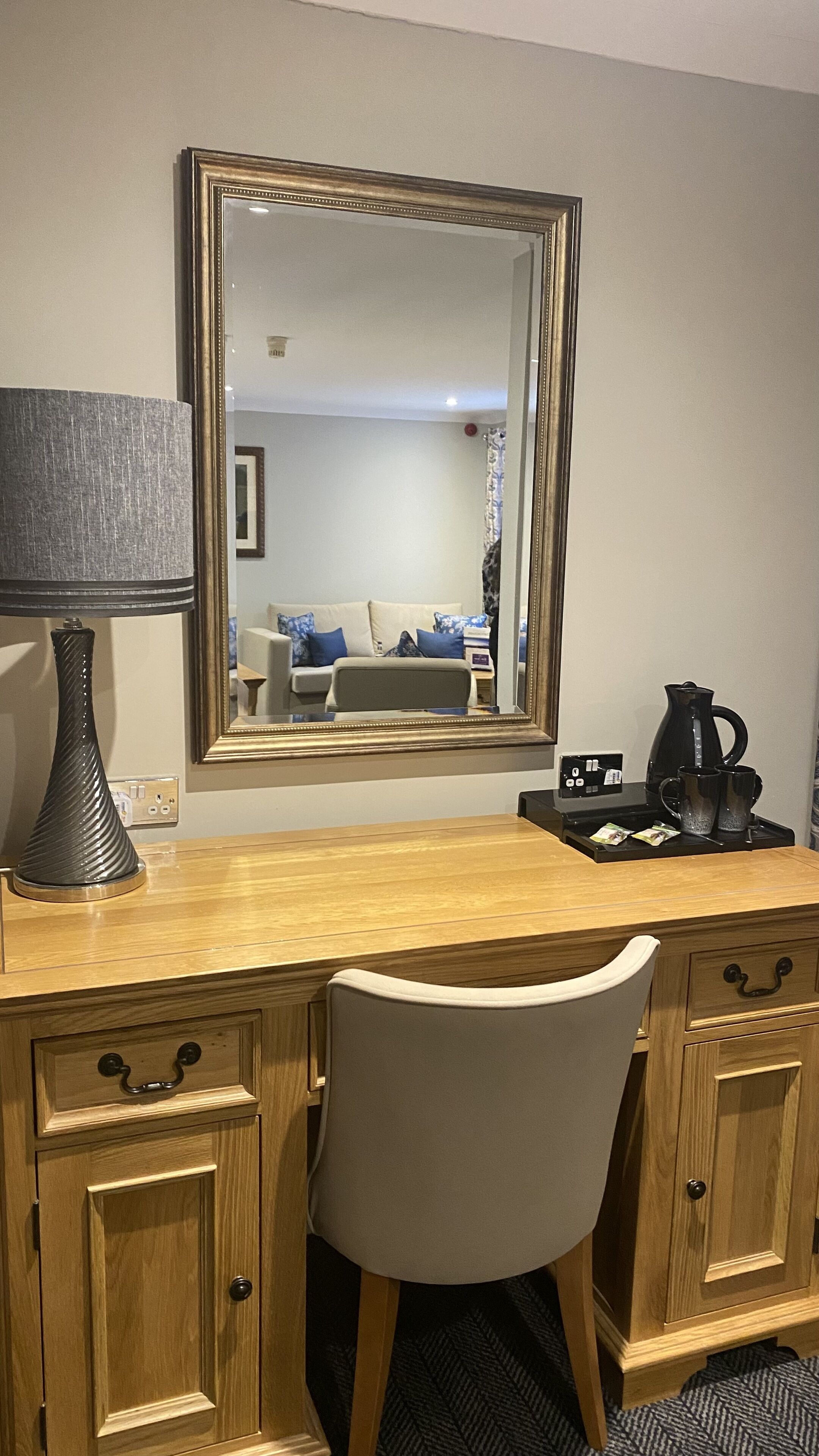 A wooden desk with a lamp, a mirror, and a coffee maker.