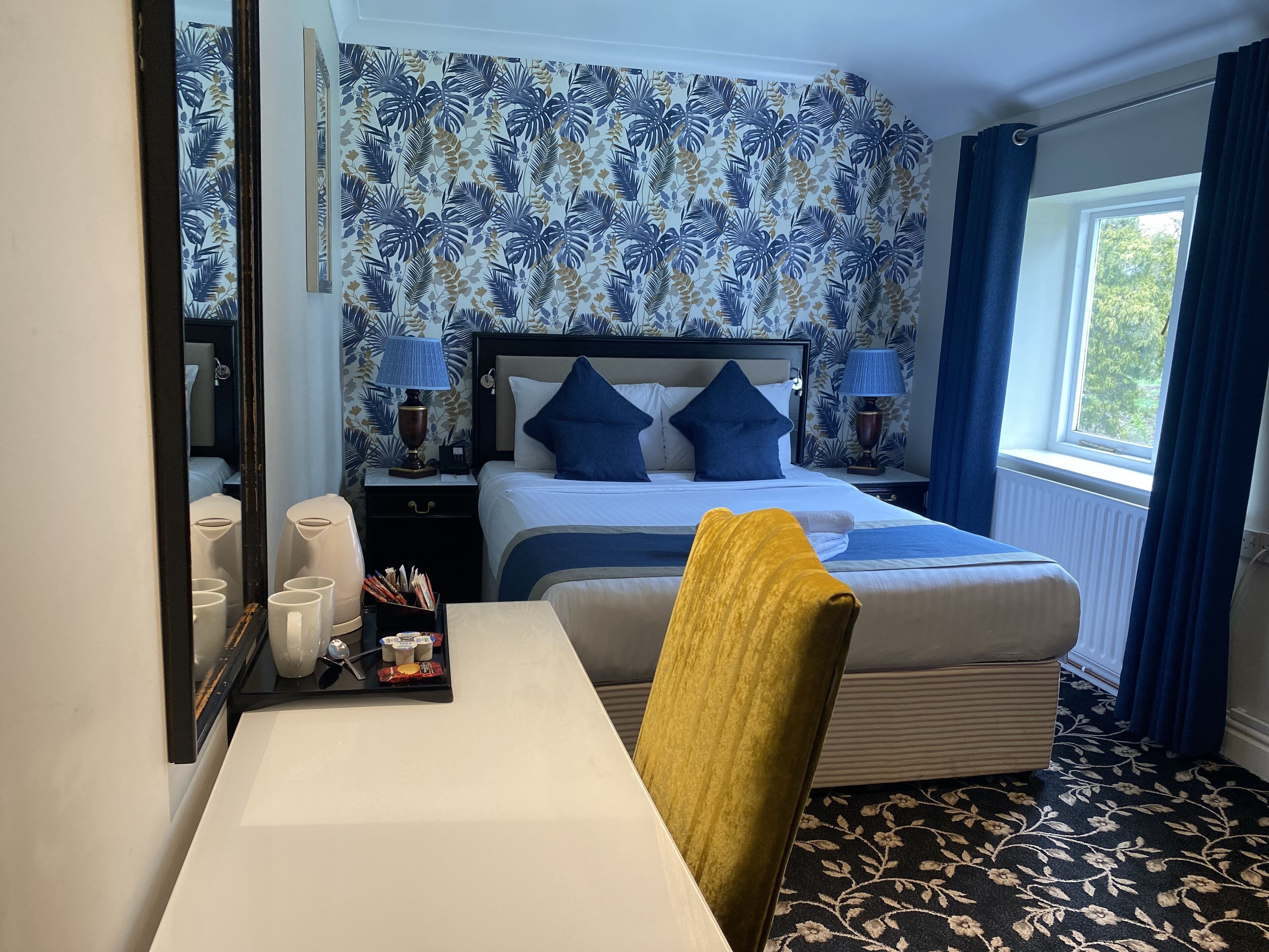 A hotel room with a bed, bedside tables, a desk, and a window with curtains.