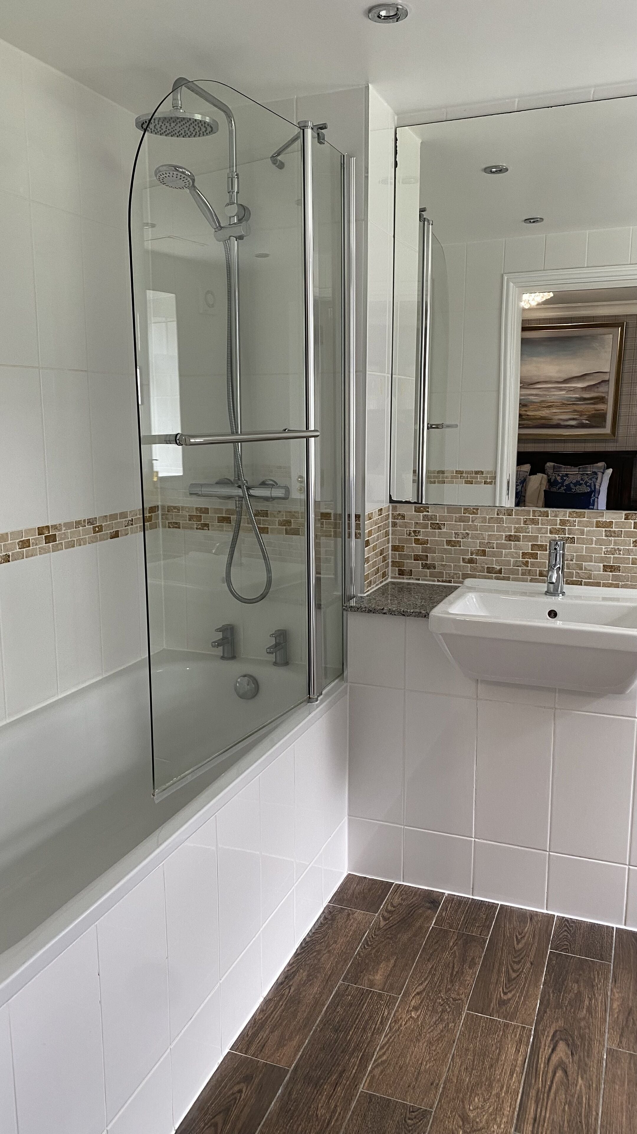 Un baño moderno con ducha de vidrio, azulejos blancos y suelo de madera.