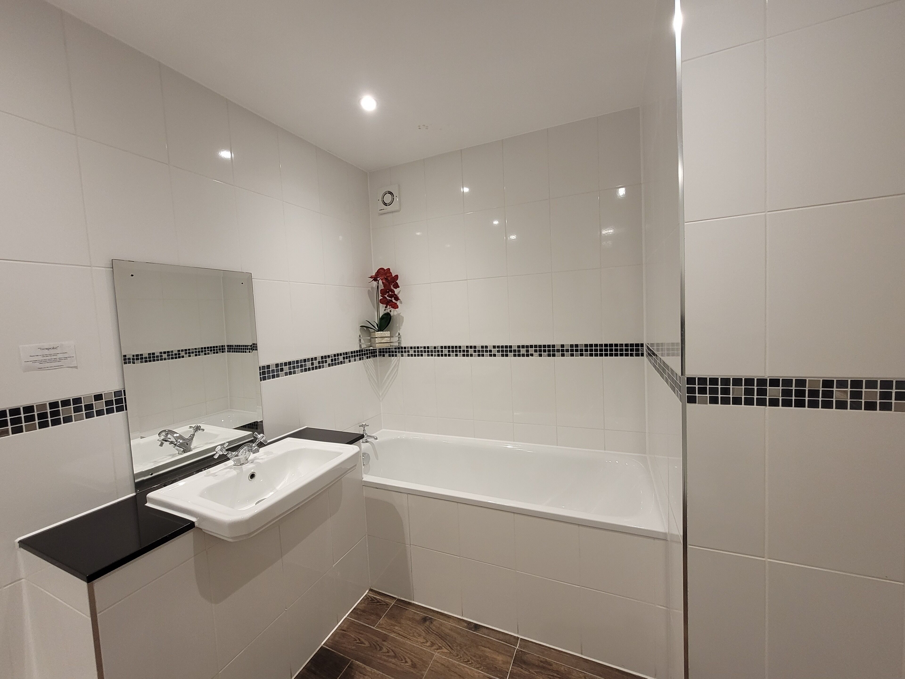 Une salle de bain moderne avec des carreaux blancs, un comptoir noir, un grand miroir, un lavabo, une baignoire et une petite plante décorative.