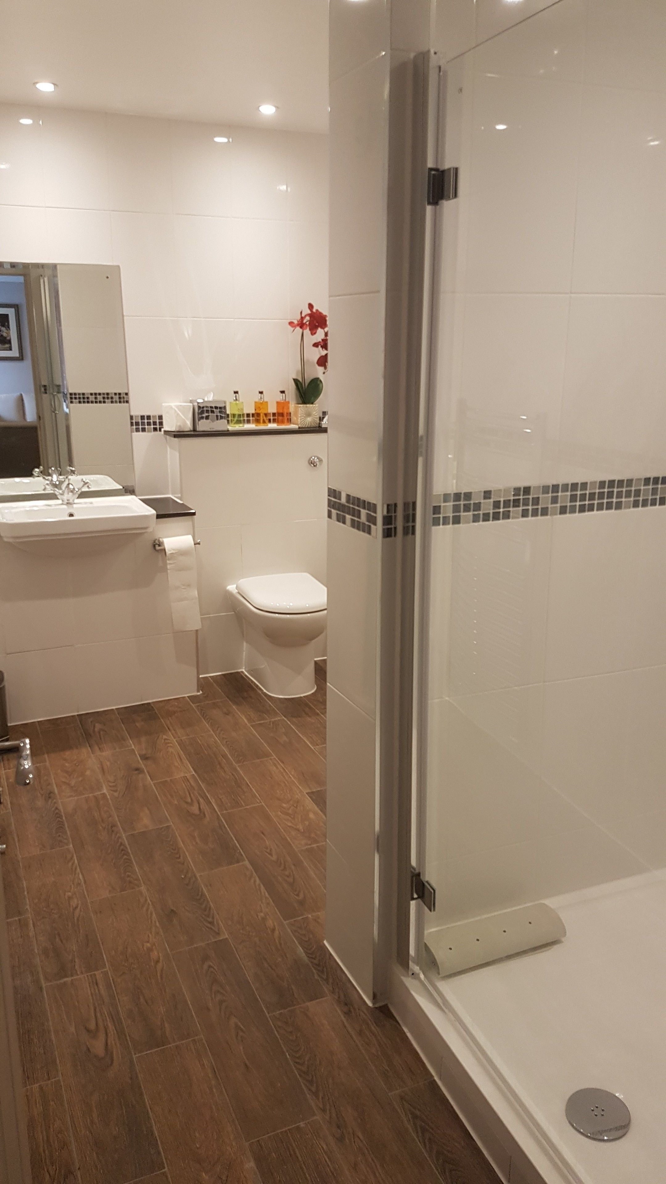 Une salle de bain moderne avec une douche à parois de verre, un lavabo blanc, des toilettes et un meuble-lavabo avec des articles de toilette.