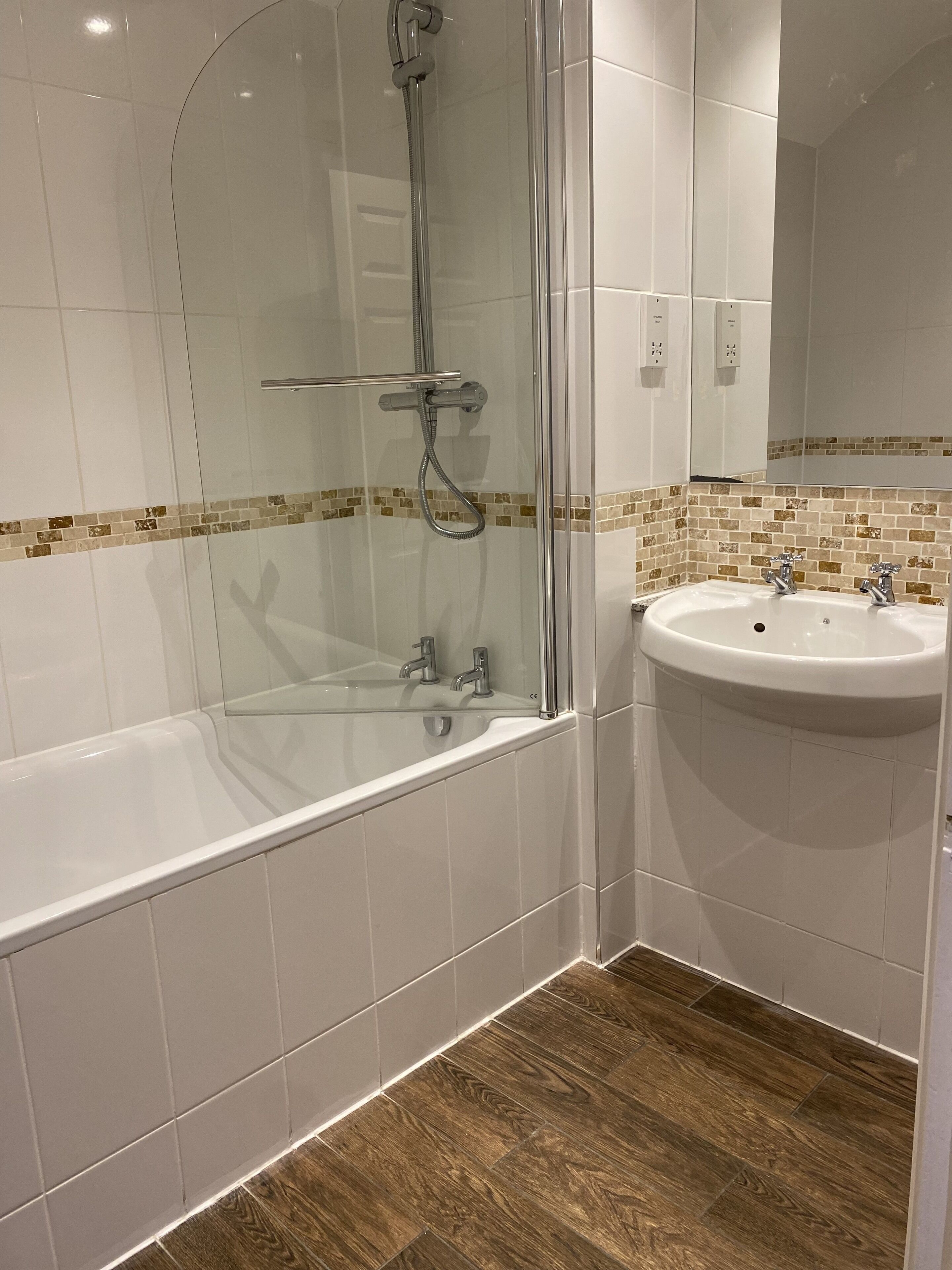 Ein modernes Badezimmer mit einer begehbaren Glasdusche, einem weißen Waschbecken und Holzboden.