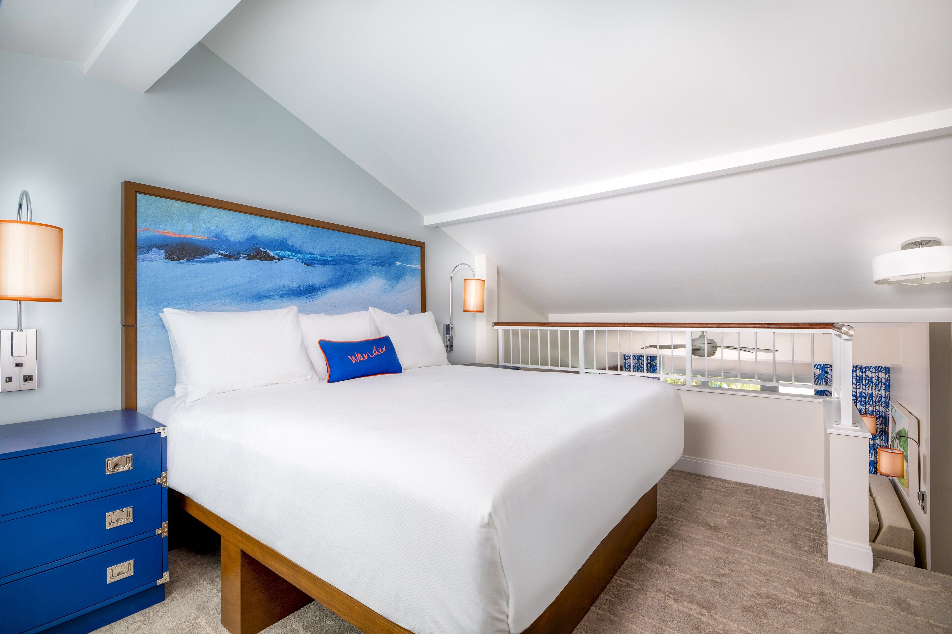 A bedroom with a large bed, a blue dresser, a painting, and a view of the outside.