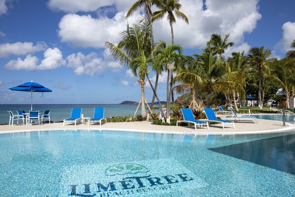 A pool area with clear blue water, lounge chairs, and palm trees.