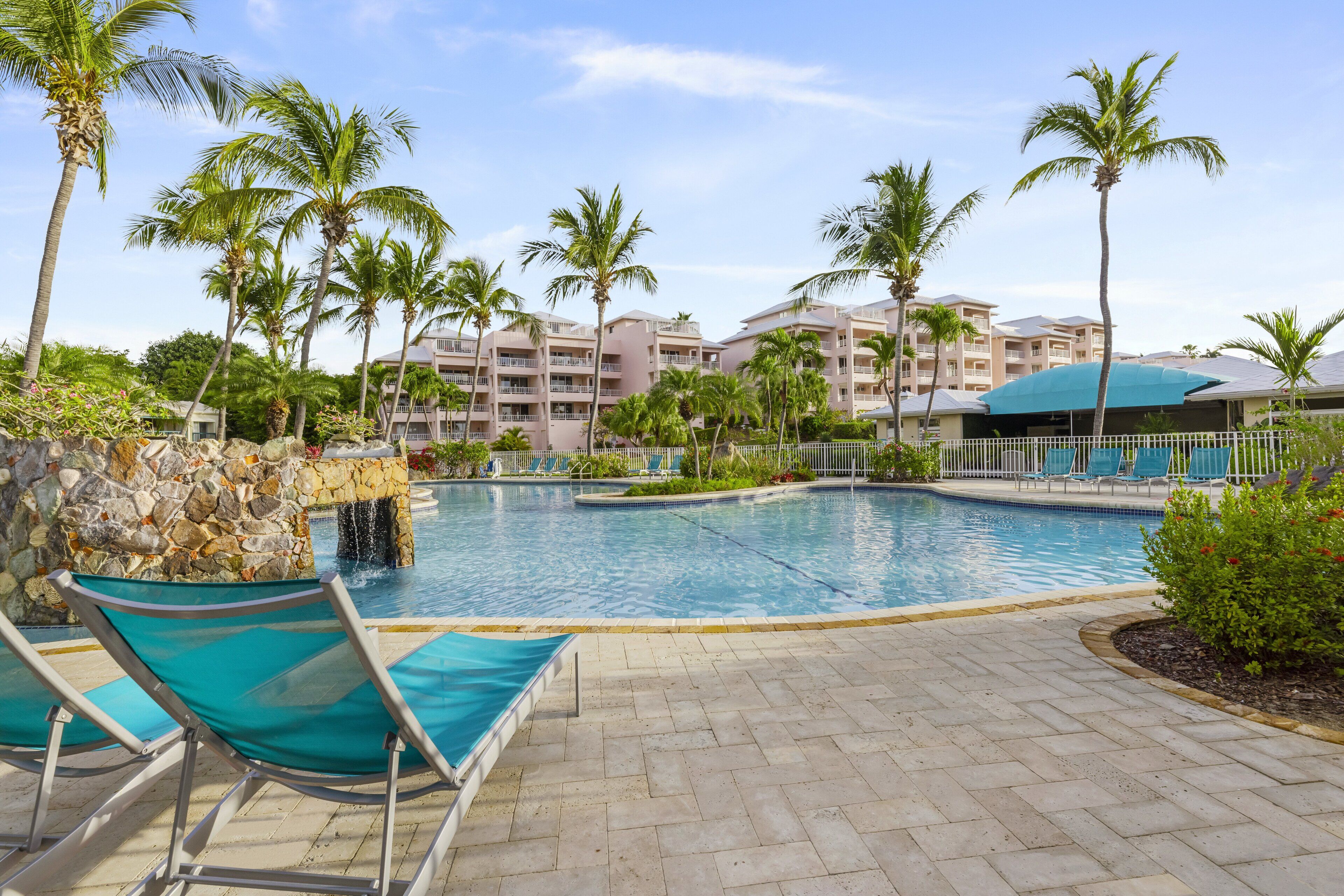 A swimming pool with lounge chairs, palm trees, and a stone wall.