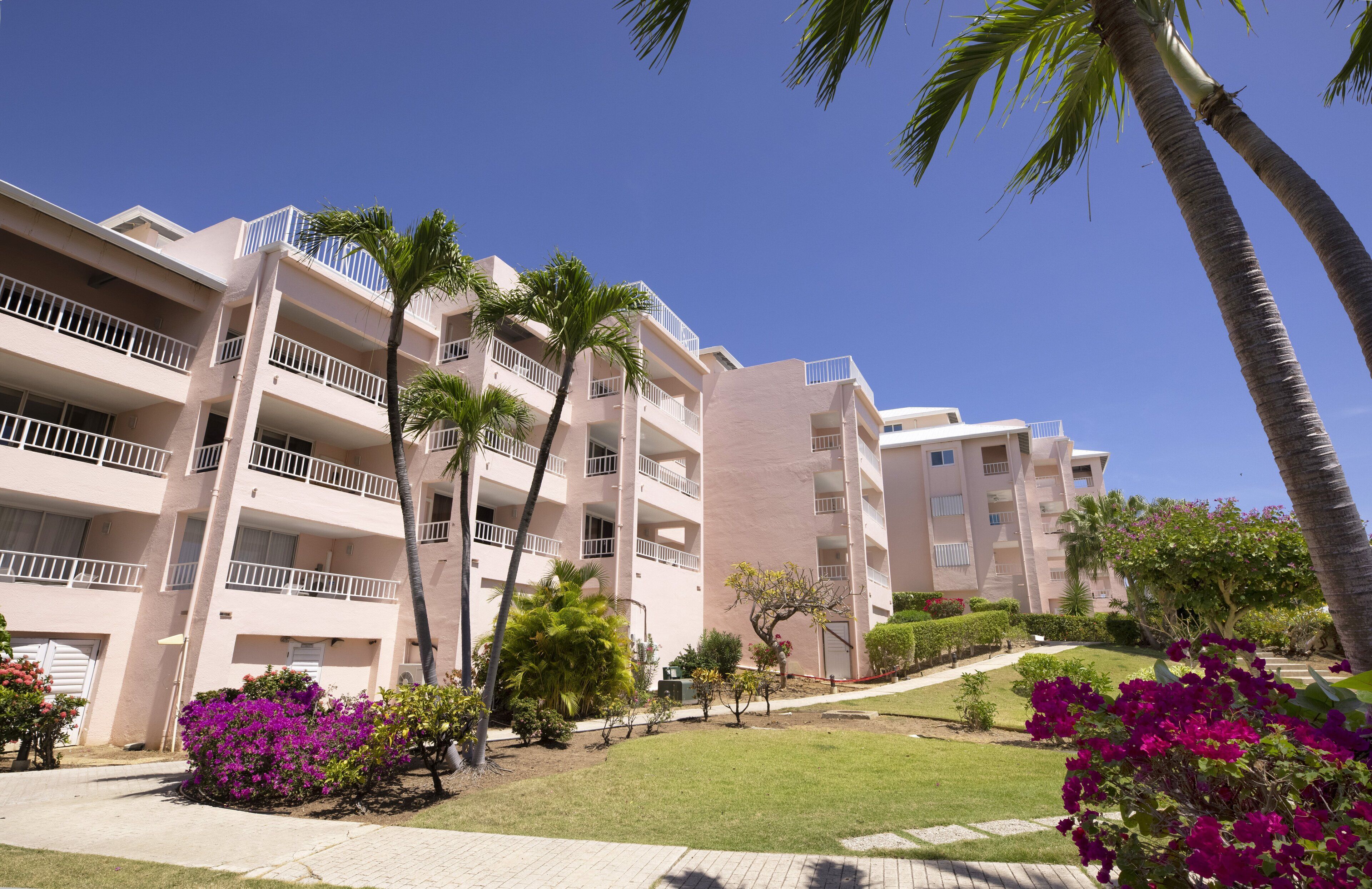 Un hotel de varios pisos con balcones, palmeras y jardines bien cuidados.