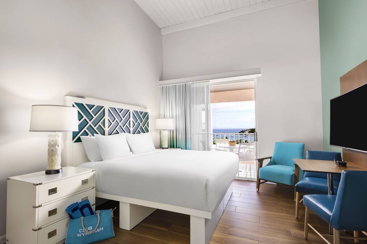 Habitación de hotel con cama, escritorio, silla, televisor y vista al océano.