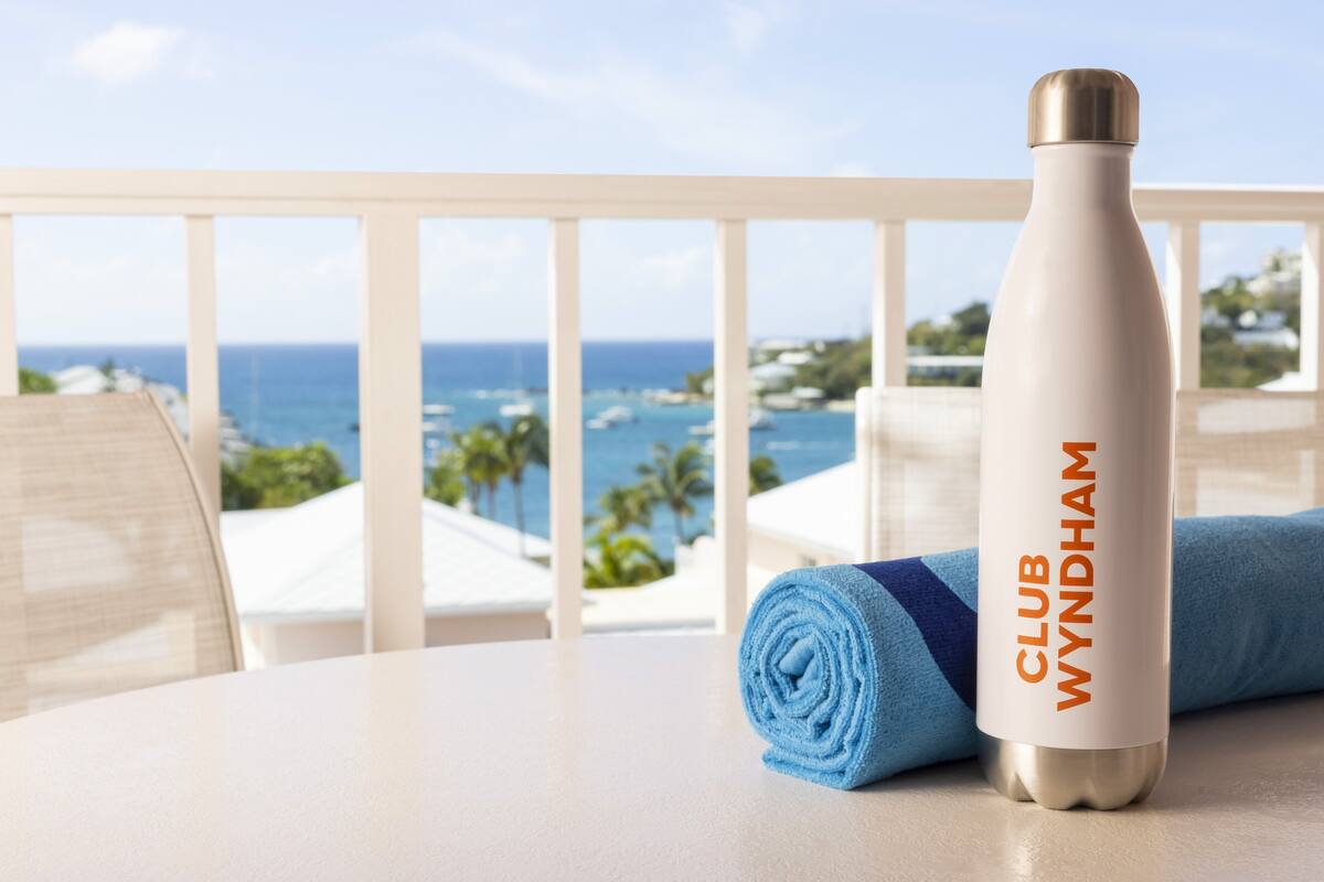 Una mesa blanca con una toalla azul enrollada y una botella de agua plateada con el texto 'CLUB WYNDHAM'.
