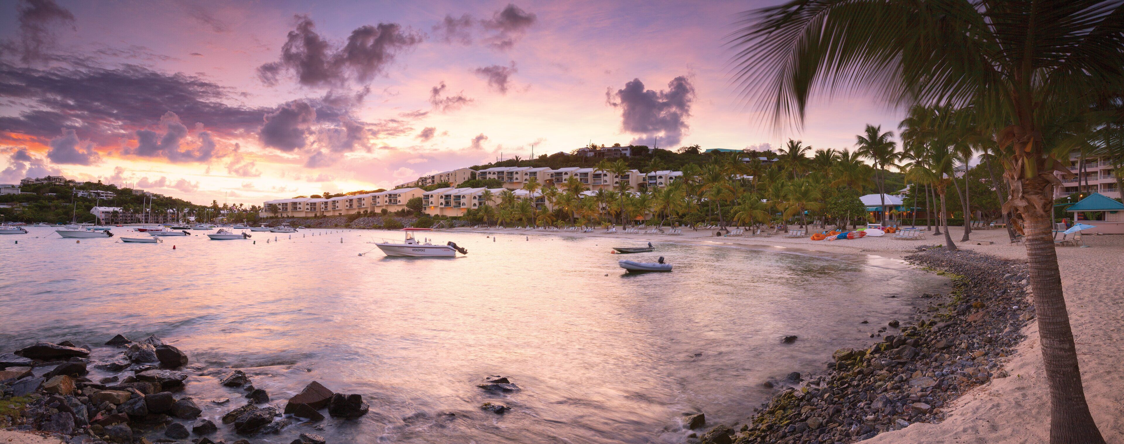A coastal resort with beachfront accommodations, boats, and palm trees.