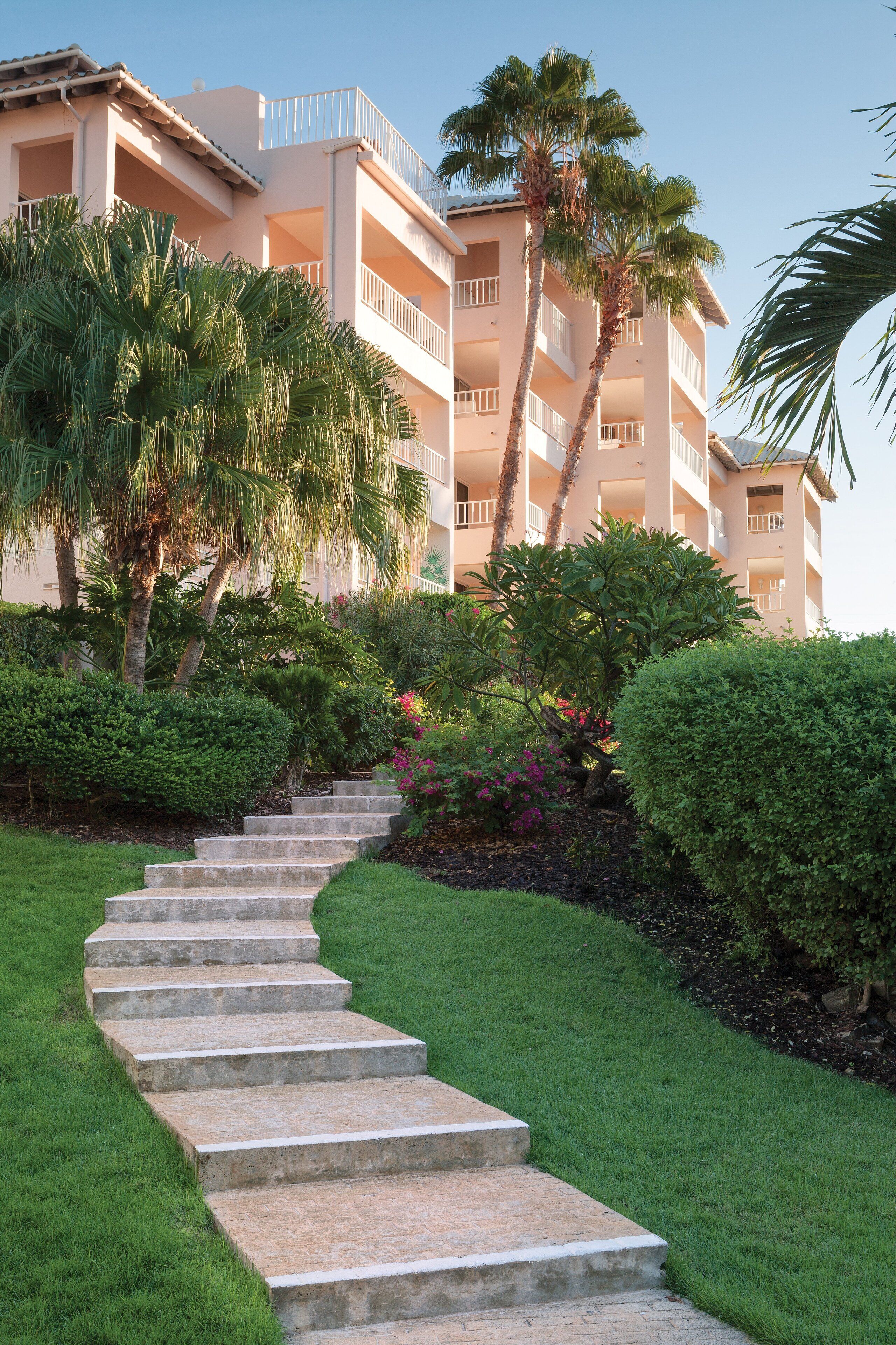A multi-story hotel with a central staircase surrounded by lush greenery and palm trees.