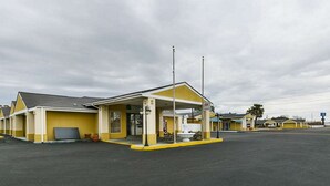 A motel with a yellow facade, a covered parking area, and a small fountain. - Rodeway Inn & Suites Enterprise (Enterprise)