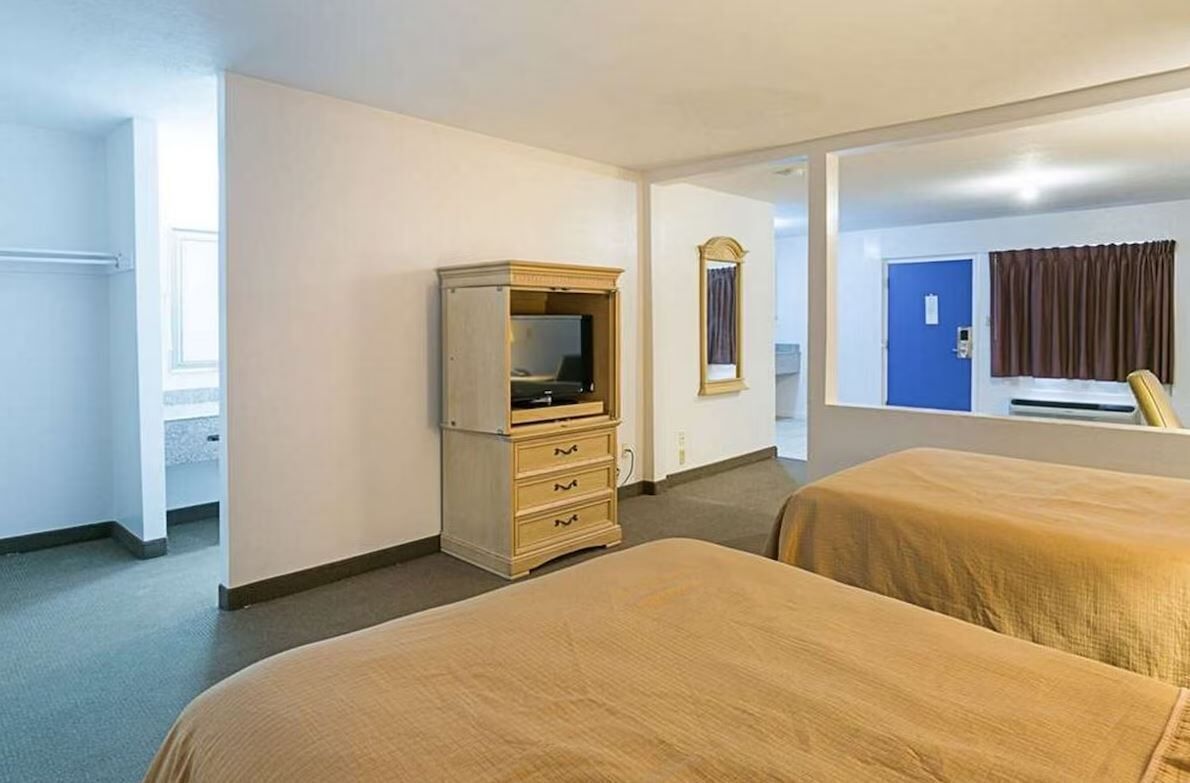 Une chambre d’hôtel avec deux lits, une commode, un miroir et une porte donnant sur une autre pièce.