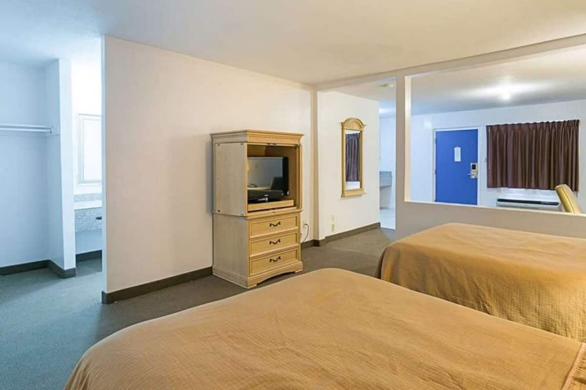 Habitación de hotel con dos camas, un aparador, un espejo y una puerta que da a otra habitación.