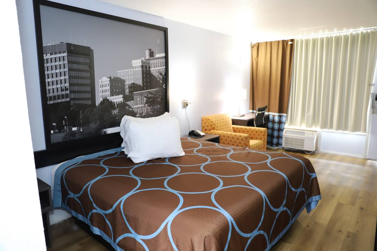 A hotel room with a large bed, a television on the wall, a desk with a chair, and a window with curtains.