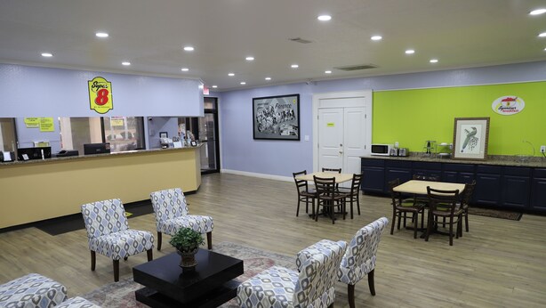 A hotel lobby with a reception desk, patterned chairs, a dining area, and a kitchen counter. - Super 8 by Wyndham Florence SC I-95 North / Hwy 76 (Florence)