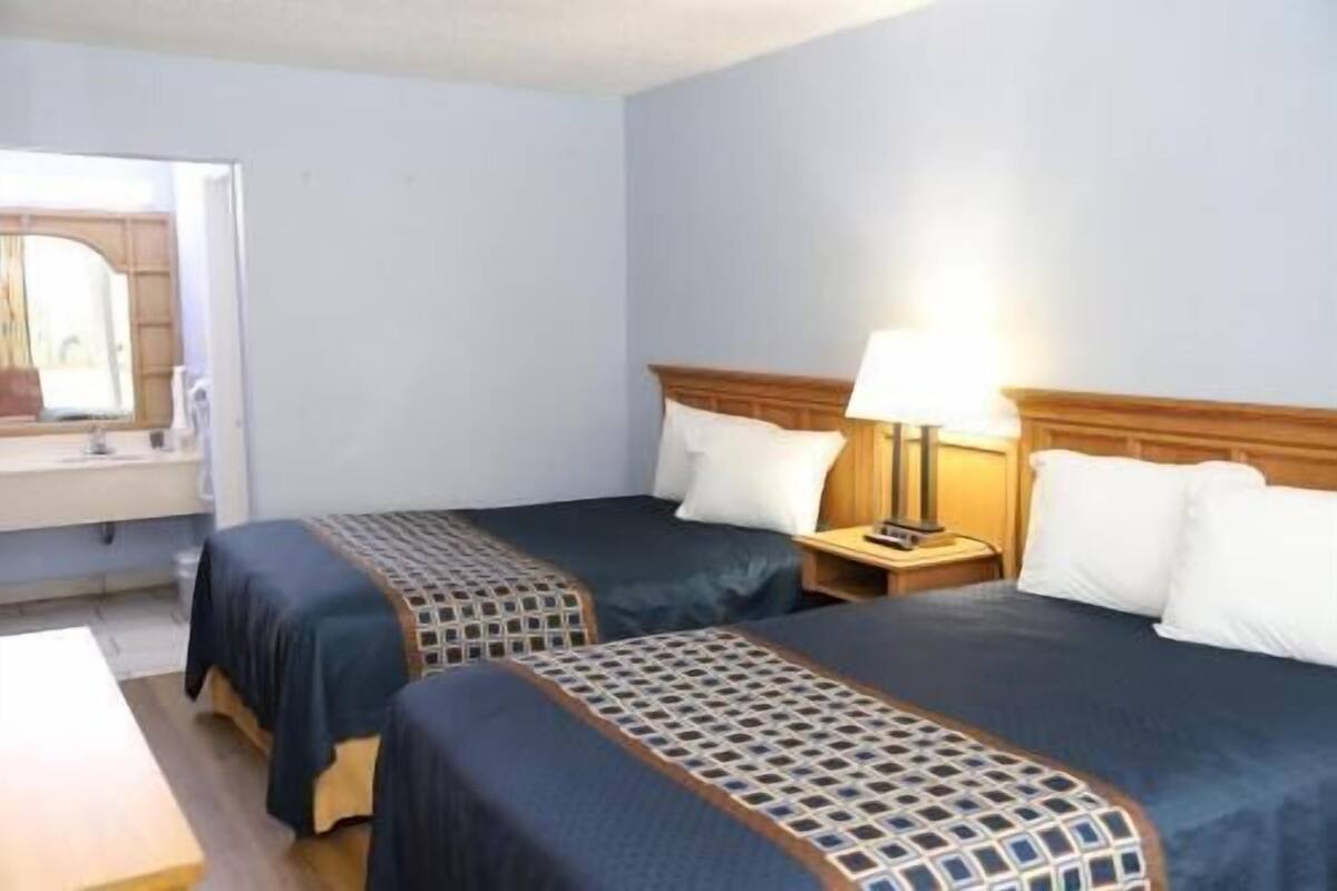 A hotel room with two beds, a nightstand with a lamp, a bathroom with a sink, and a mirror.