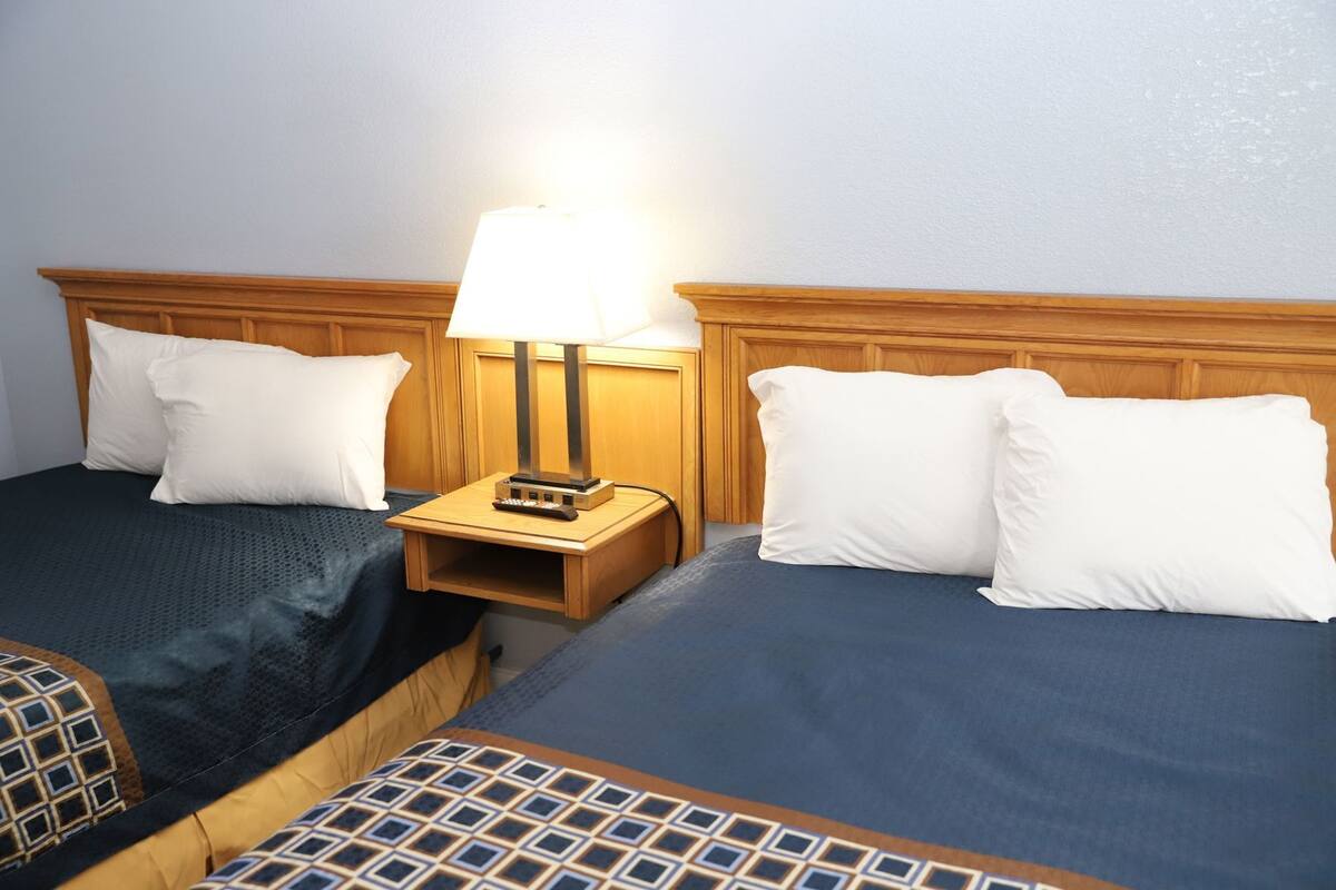 A hotel room with two beds, a nightstand with a lamp, and a small table.