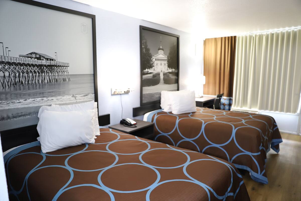 A hotel room with two beds, a nightstand, a desk, and a large framed picture on the wall.