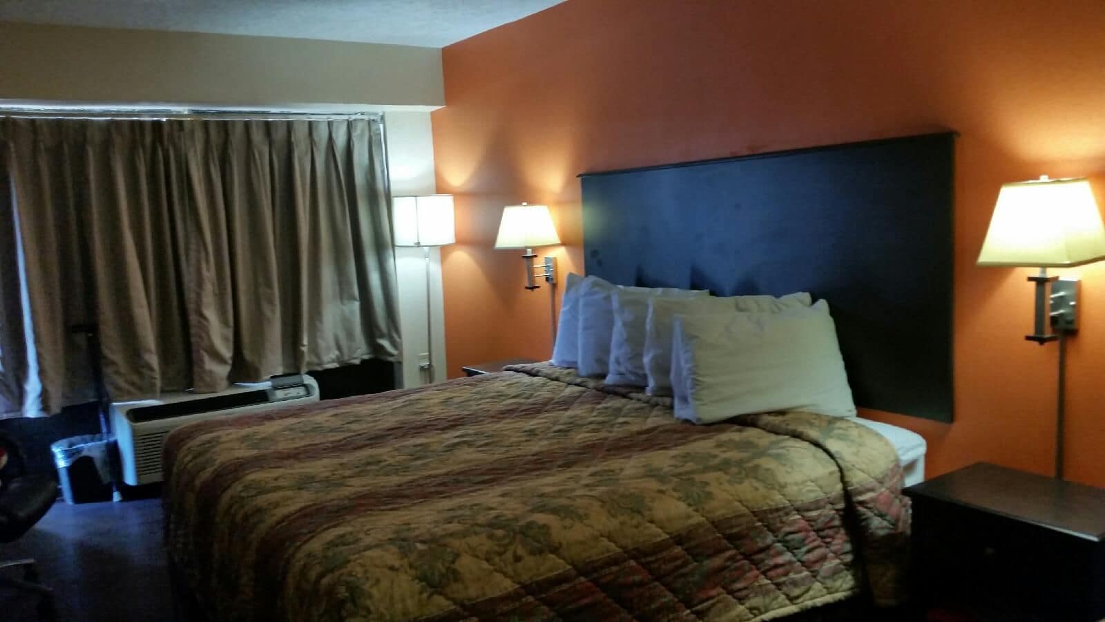 A hotel room with a bed, two bedside lamps, a headboard, and a window with curtains.