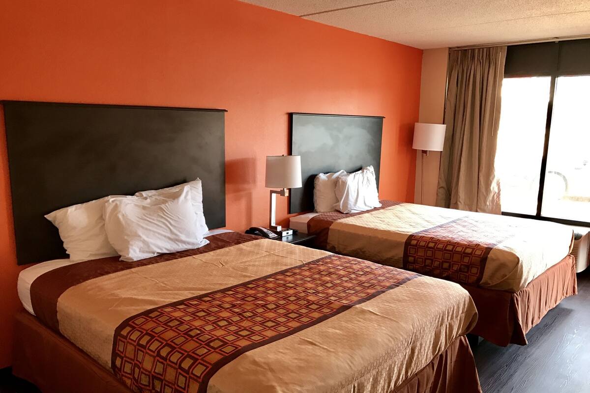 Habitación de hotel con dos camas, cada una con cabecera, lámparas de noche y un ventanal con cortinas.