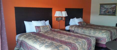 Una habitación de hotel con dos camas, cada una con una colcha estampada y almohadas blancas. Hay una mesita de noche con una lámpara entre las camas.