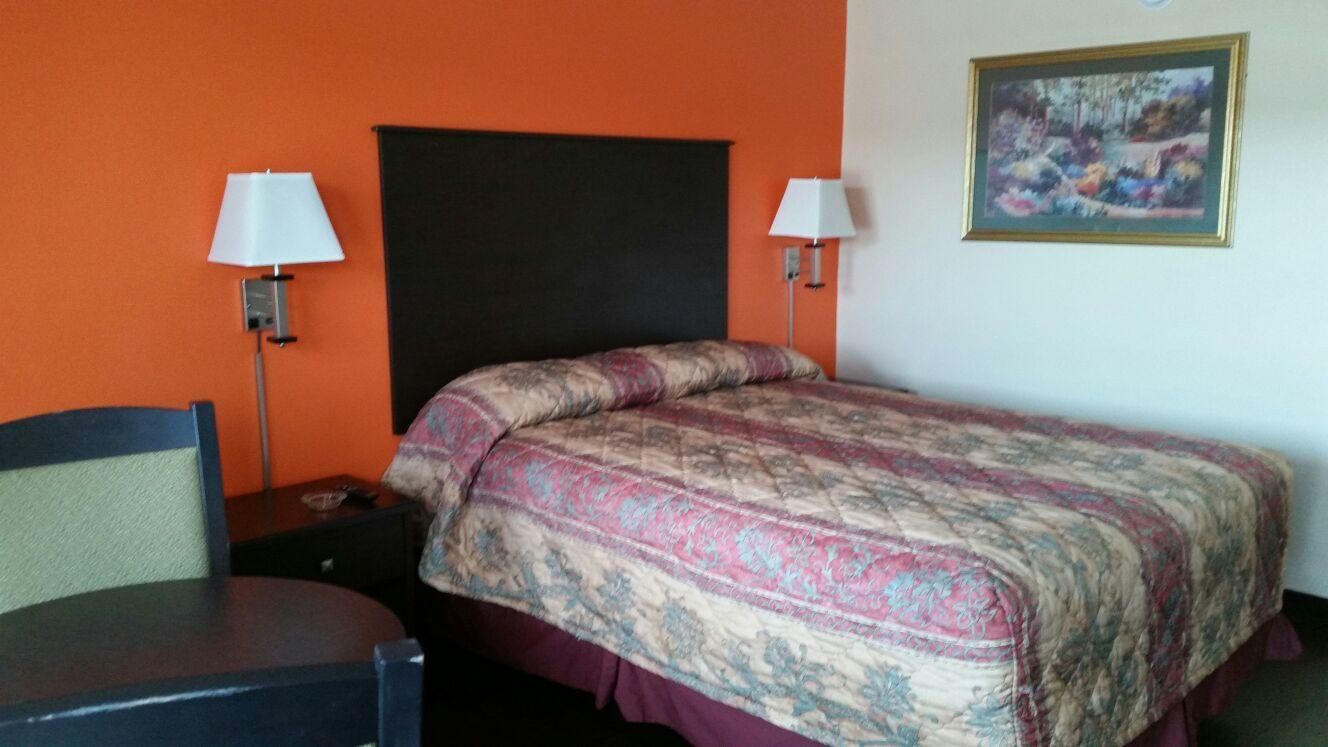 A hotel room with a bed, two bedside lamps, a chair, and a painting on the wall.