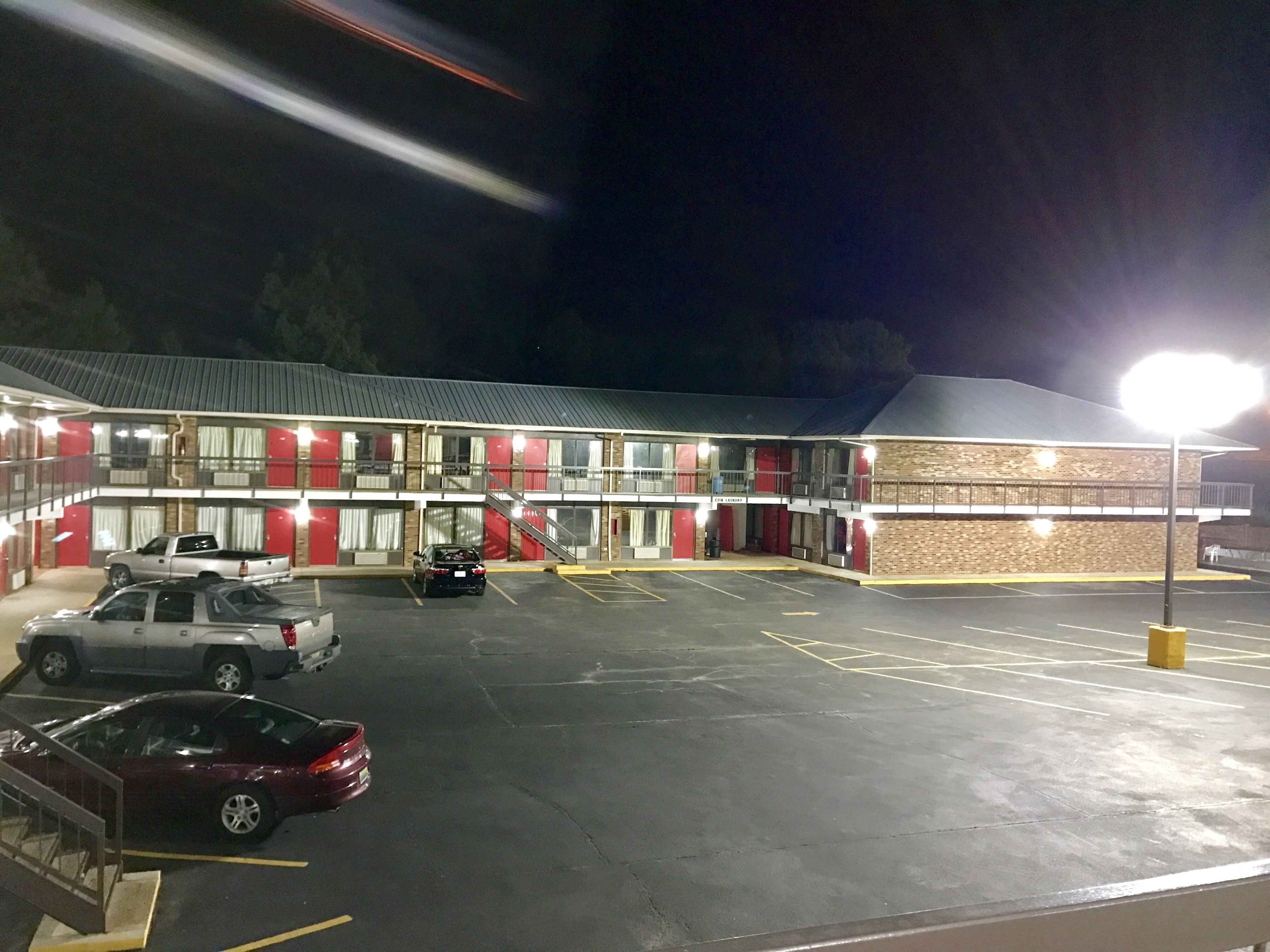 A motel with a two-story structure, a parking lot with several cars, and a well-lit exterior.
