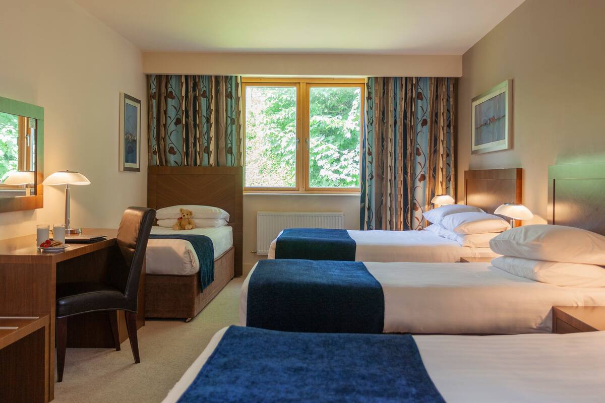 A hotel room with two beds, a desk, a chair, and a window with curtains.
