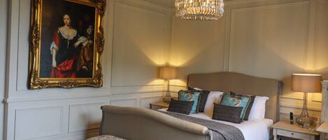 A bedroom with a large bed, a bench, a chandelier, and a painting on the wall.
