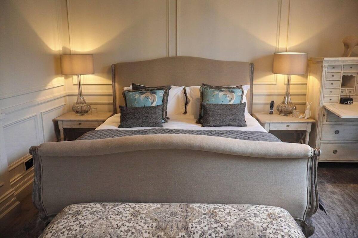 A bed with a headboard, two bedside tables with lamps, a dresser, and a patterned bench.