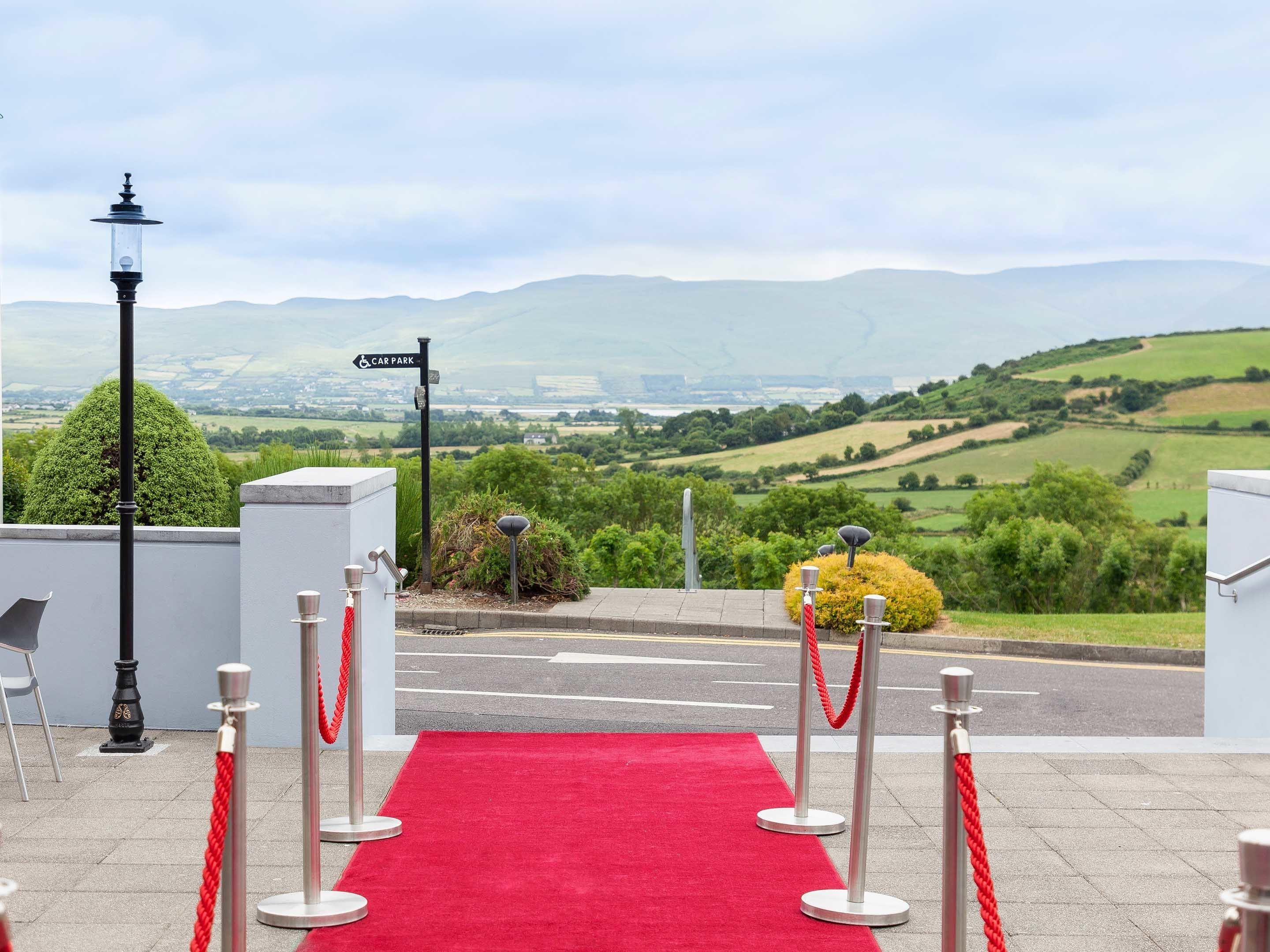 A red carpet leading to a car park with a scenic view of hills and fields.