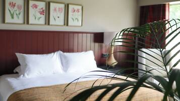 A hotel room with a bed, a large potted plant, and framed floral artwork on the wall.