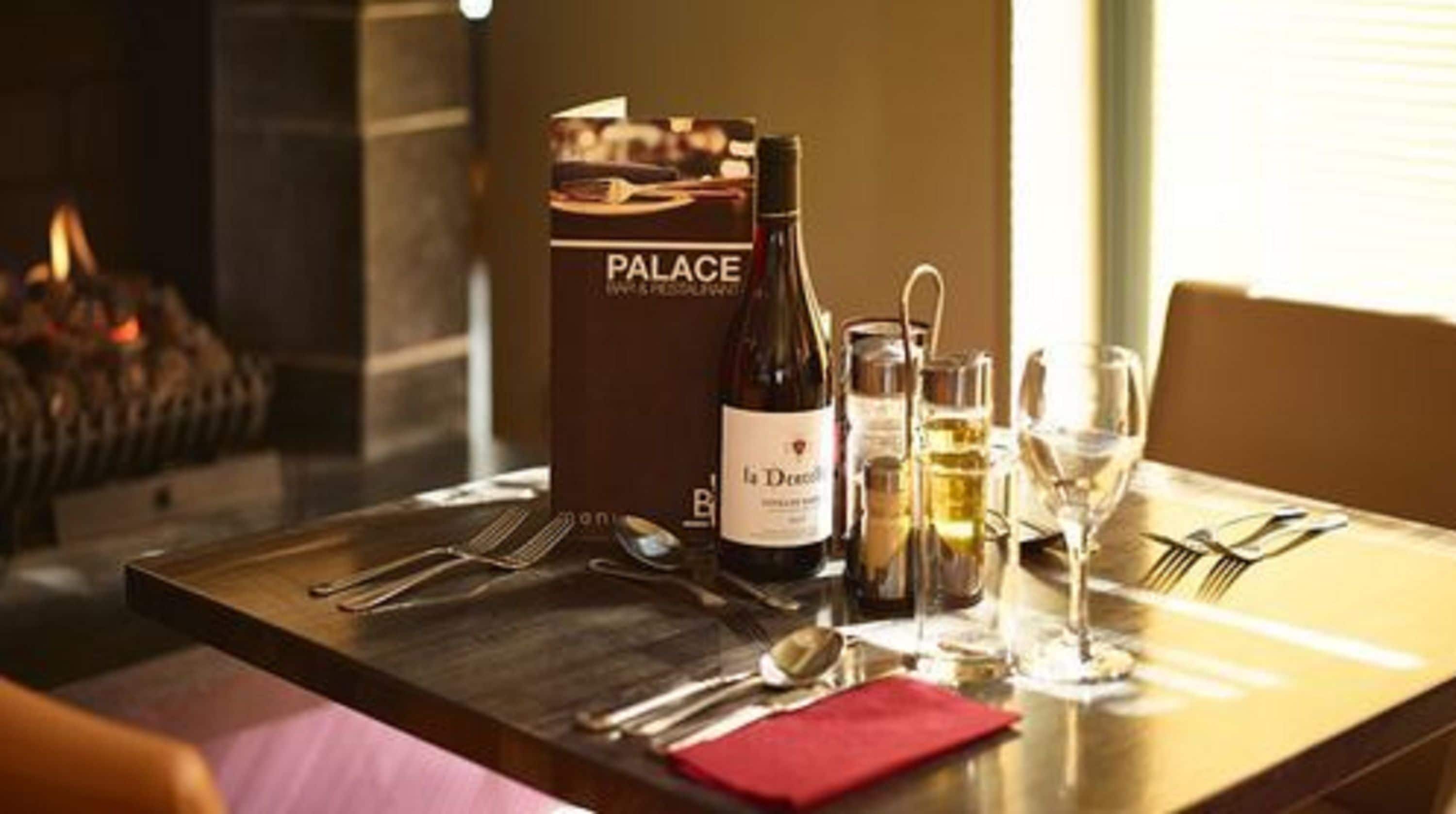 A dining table set with a bottle of wine, glasses, cutlery, and a menu titled "PALACE".