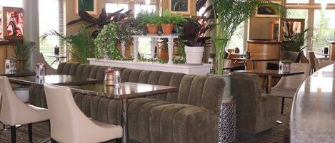 Un restaurante con zona de estar con cojines verdes, sillas blancas y una variedad de plantas en macetas.
