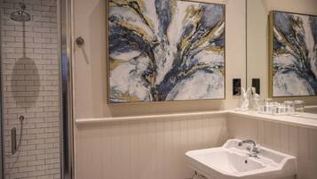 A bathroom with a shower, a sink, and two large abstract paintings on the wall.