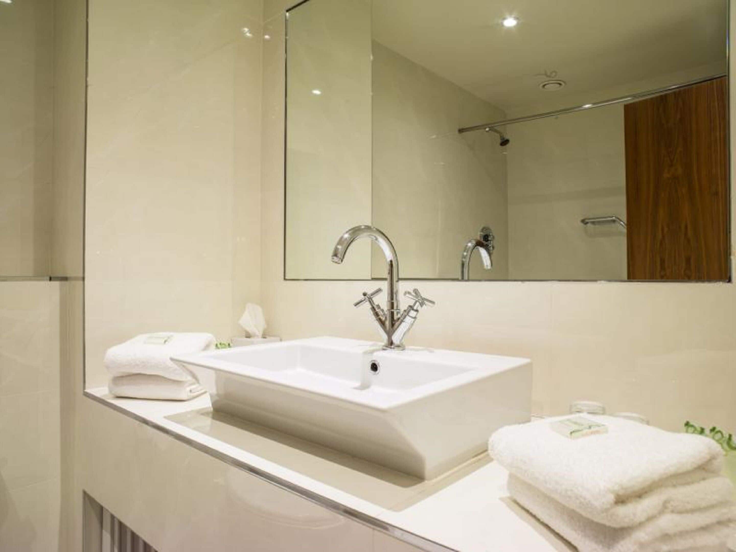 Un baño moderno con un lavamanos grande rectangular, un espejo y un panel de madera en la pared.