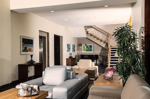 Una sala de estar moderna con una escalera, sofás de cuero, una mesa de centro y una planta grande.